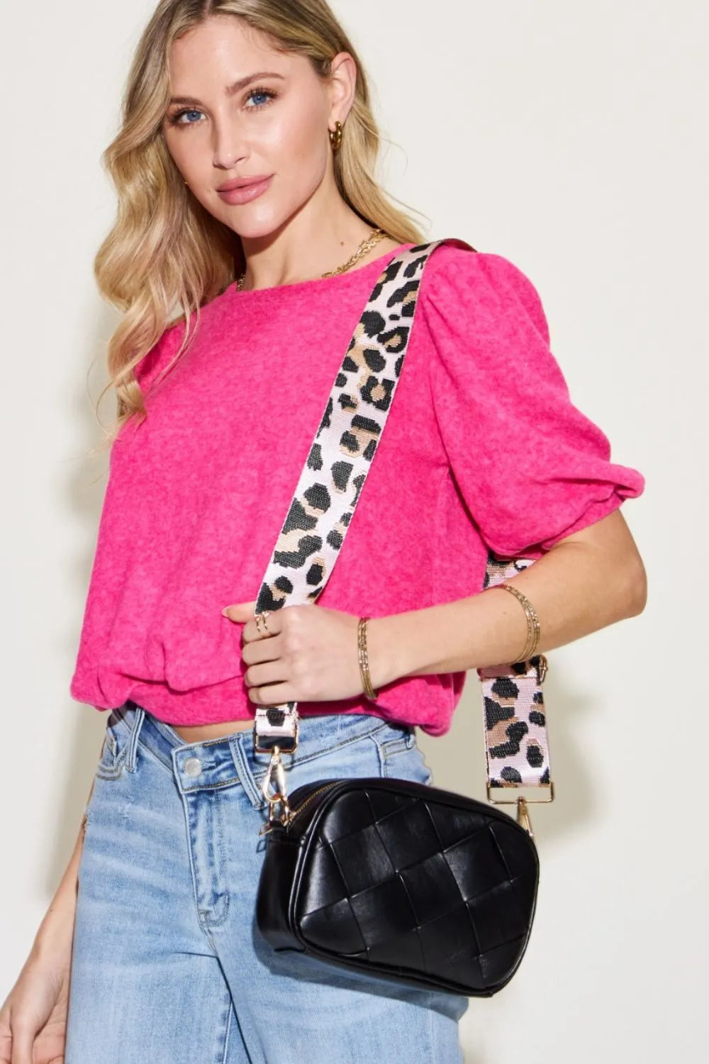 A woman carrying a trendy black bag with leopard print strap.