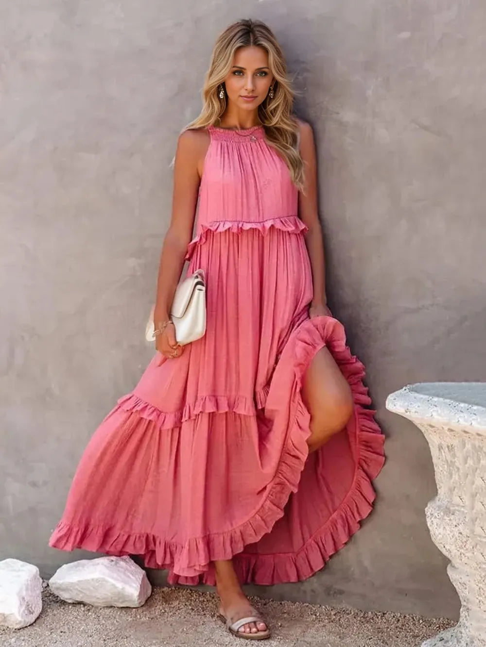 A woman wearing multi frilled pink maxi dress holding a white purse.  